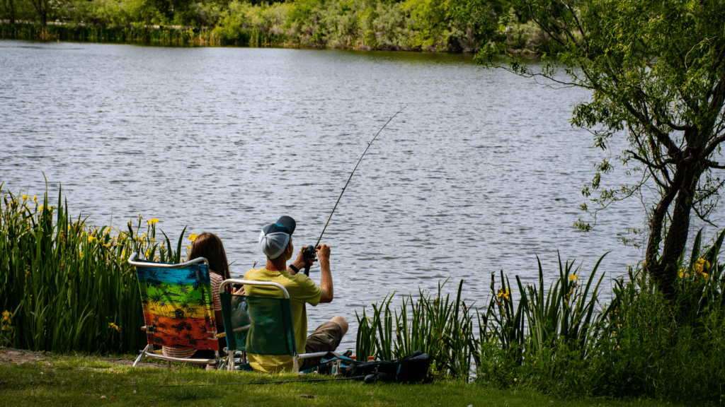 A person is holding a fishing rod and smiling while standing in front of a lake