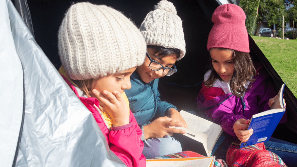 three children sitting in a tent reading books