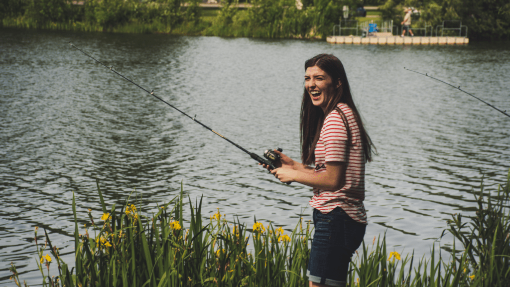 A person is holding a fishing rod and smiling while standing in front of a lake