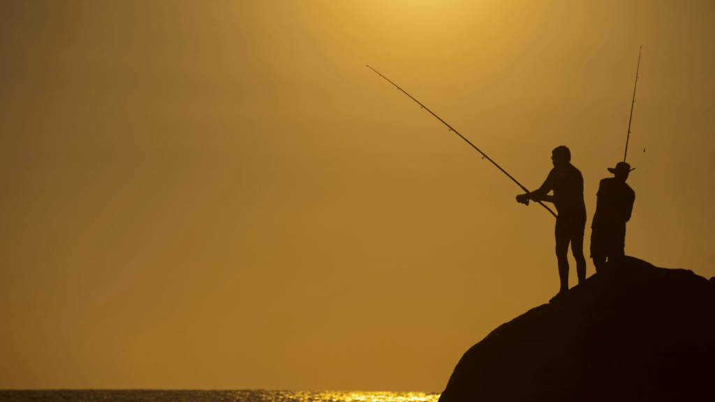 silhouette of two individuals fishing on the beach at sunset