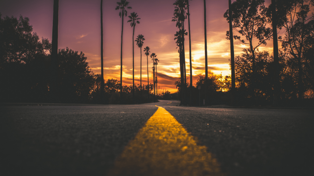 an empty road with the sun setting behind it