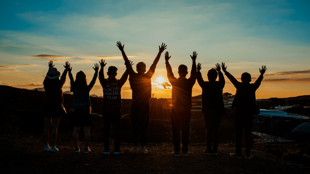 silhouette of a group of person with their hands up in the air at sunset