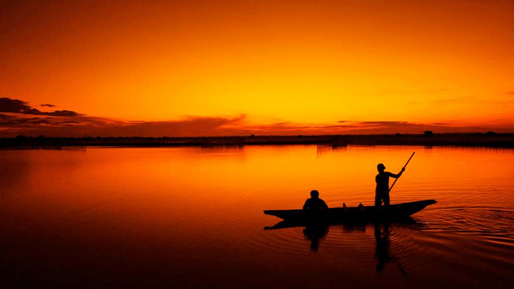 silhouette of two individuals fishing on the beach at sunset