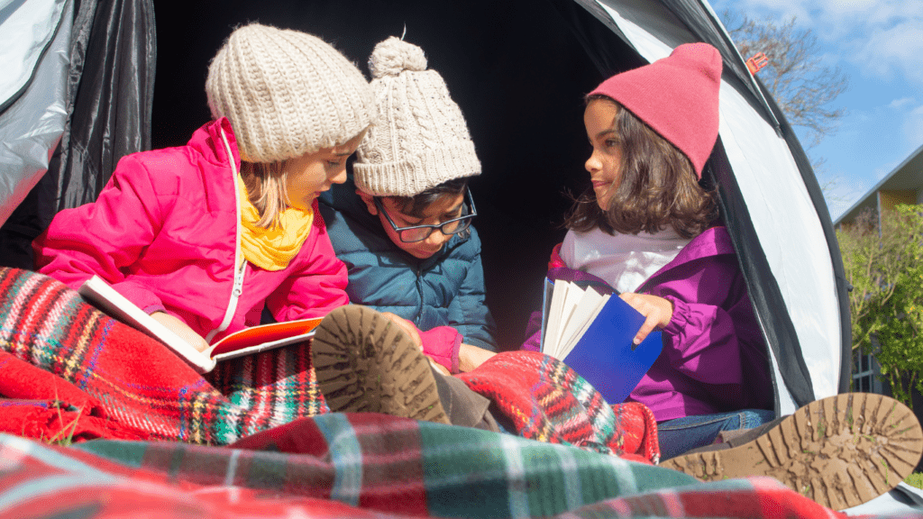 three children sitting in a tent reading books